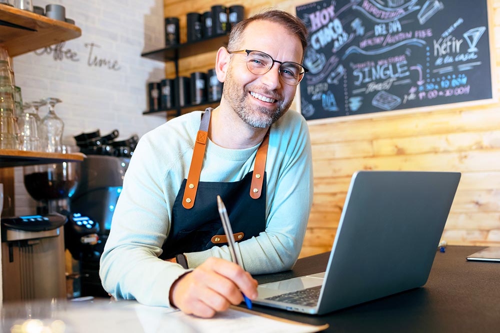 Shot of handsome mature owner bakery working while analyzing report for order delivery with laptop in a pastry shop.